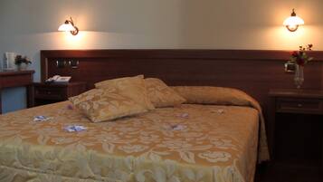 Un letto rifatto con una coperta a fiori e due cuscini, affiancato da comodini con lampade e un vaso di fiori.