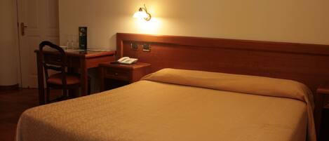 A hotel room with a bed, a desk with a telephone, and a wall-mounted light.