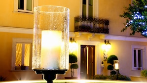 Un espacio al aire libre iluminado con velas, con vista despejada a la fachada de un edificio, incluyendo ventanas y un balcón.