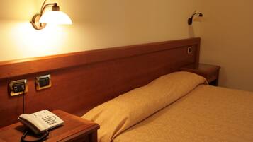 Quarto de hotel com cabeceira de madeira, mesa de cabeceira com telefone e luminária fixada na parede.