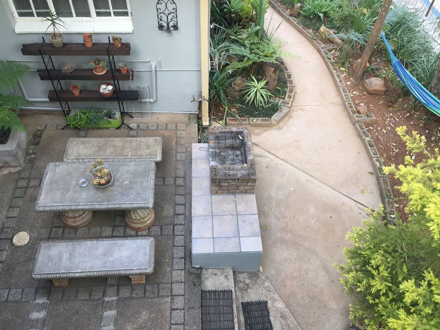 A patio area with a concrete table and benches, surrounded by potted plants and a brick barbecue grill.