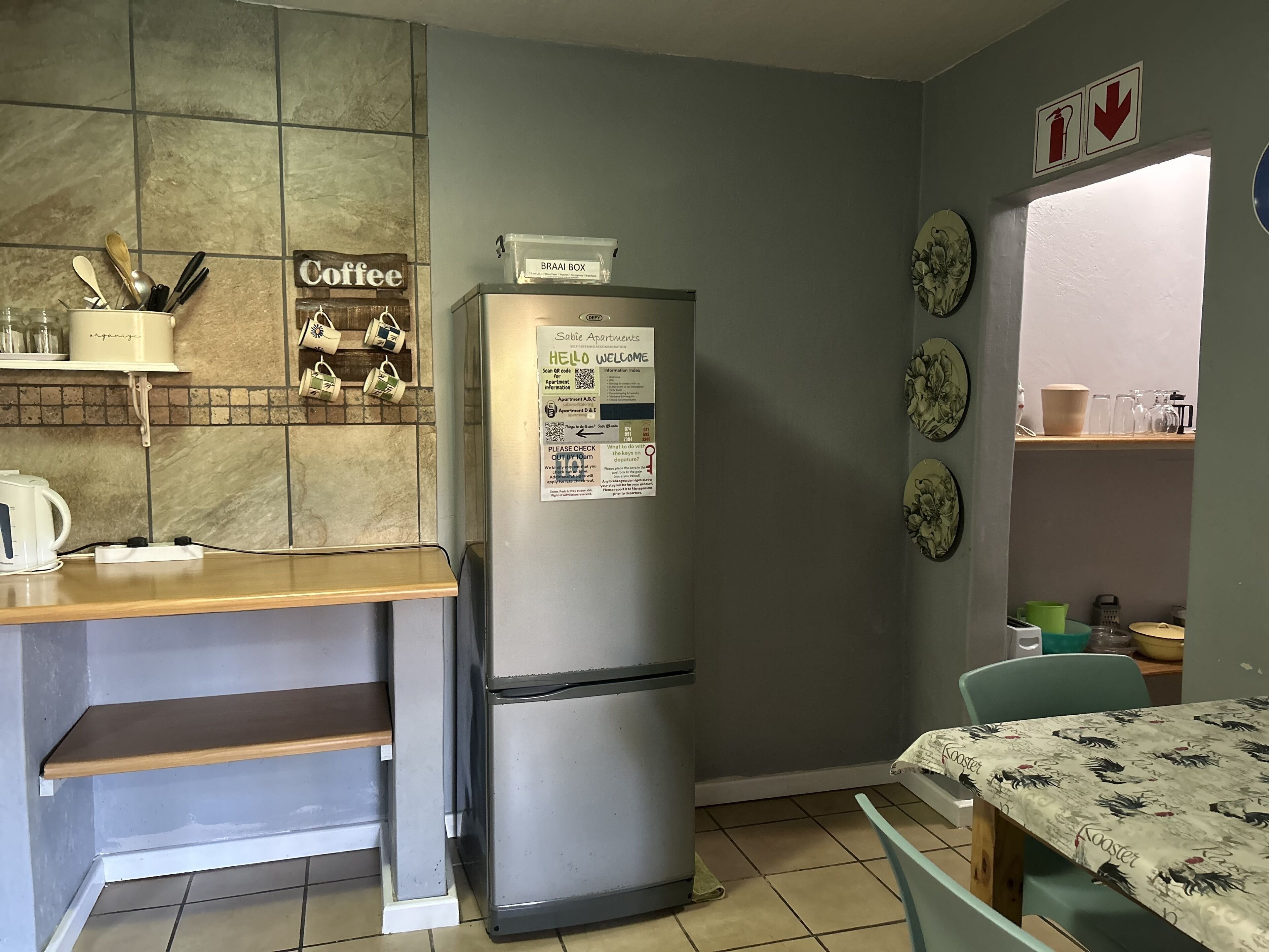 Une cuisine compacte dotée d’un réfrigérateur en acier inoxydable, d’un mur décoré sur le thème du café et d’un coin repas avec une table et des chaises.