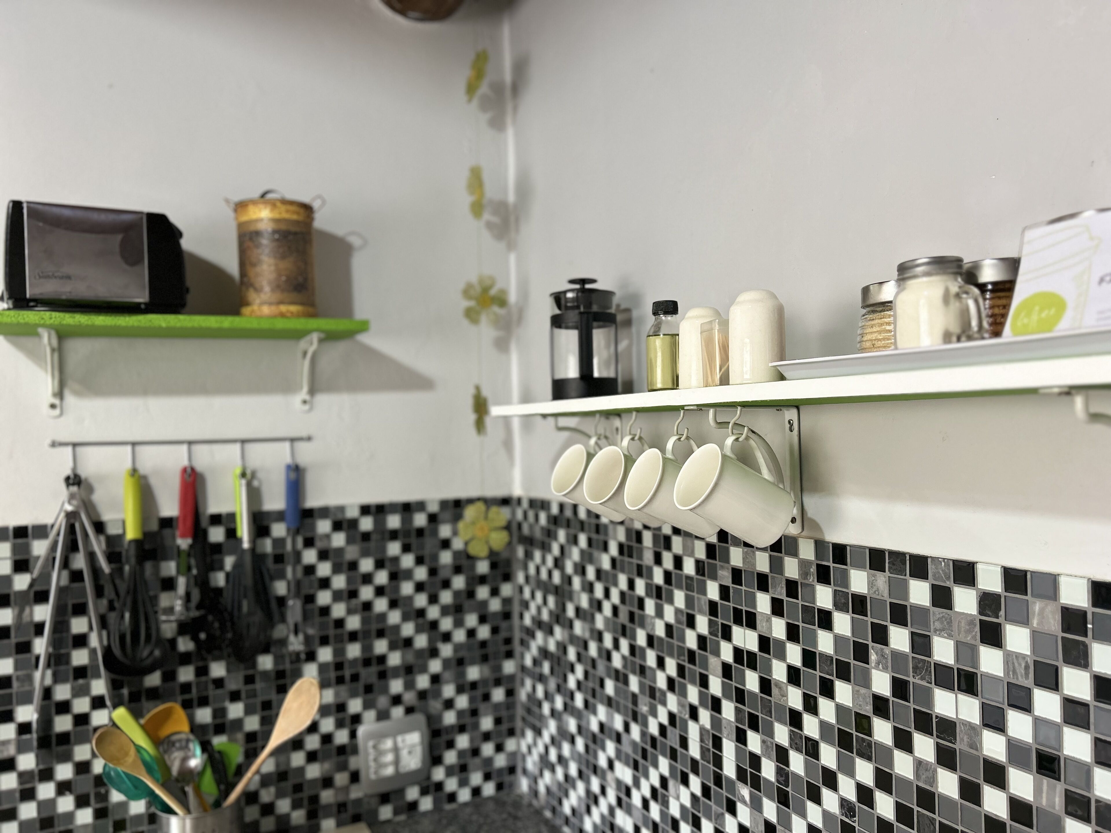 A kitchen with a checkered backsplash, hanging utensils, and shelves with kitchenware.