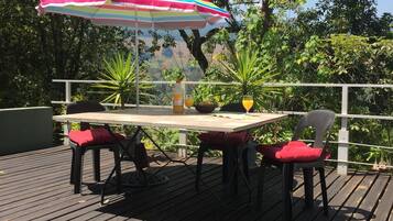 Une terrasse en bois avec une table et des chaises, un parasol rayé aux couleurs vives et des plantes en pot.