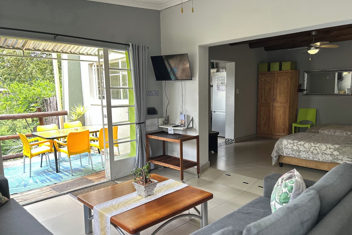 A modern room with a sofa, a dining table with yellow chairs, a TV, a ceiling fan, and a view of the outdoors.