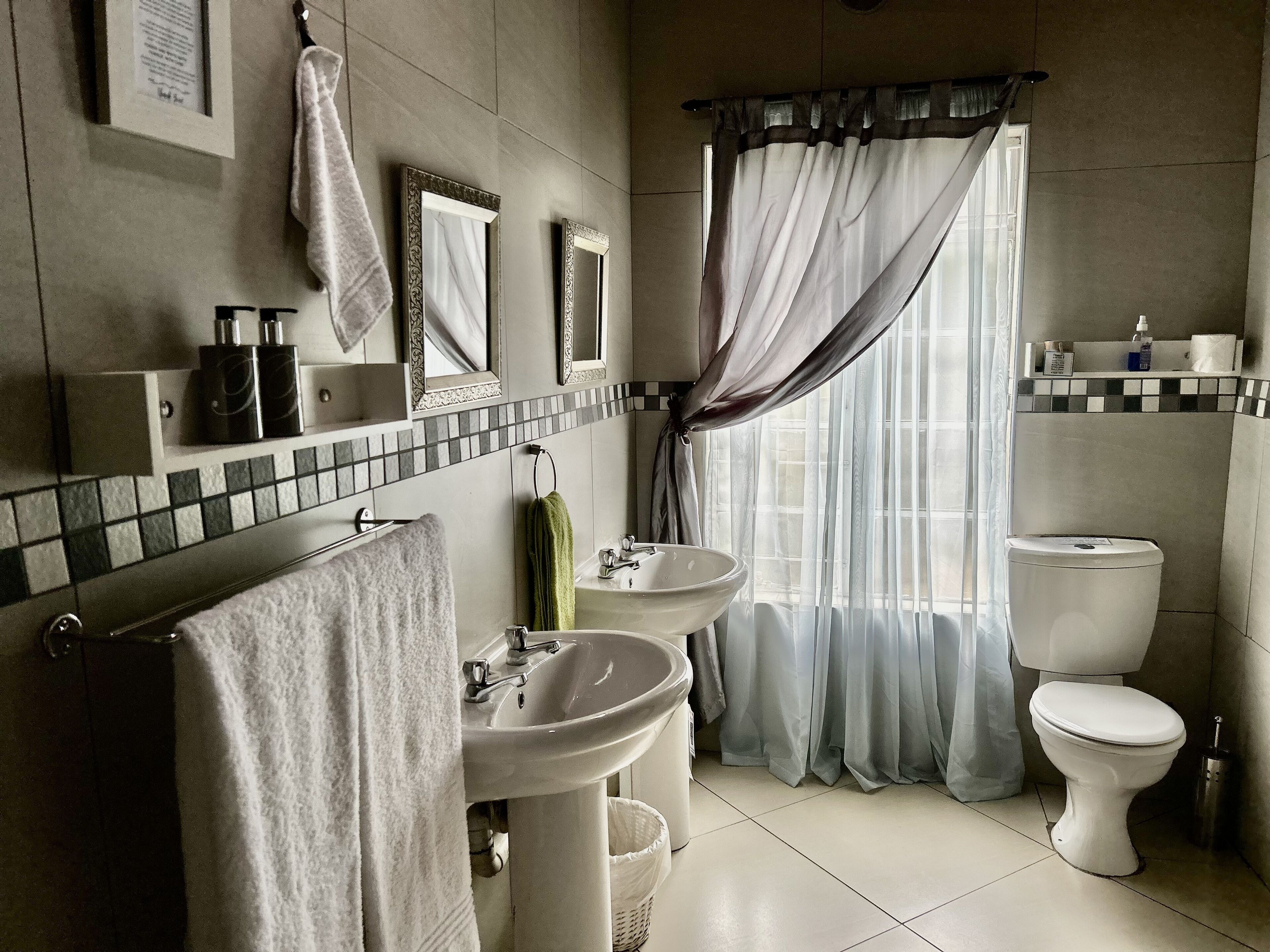 A bathroom with two sinks, a toilet, and a window with curtains.
