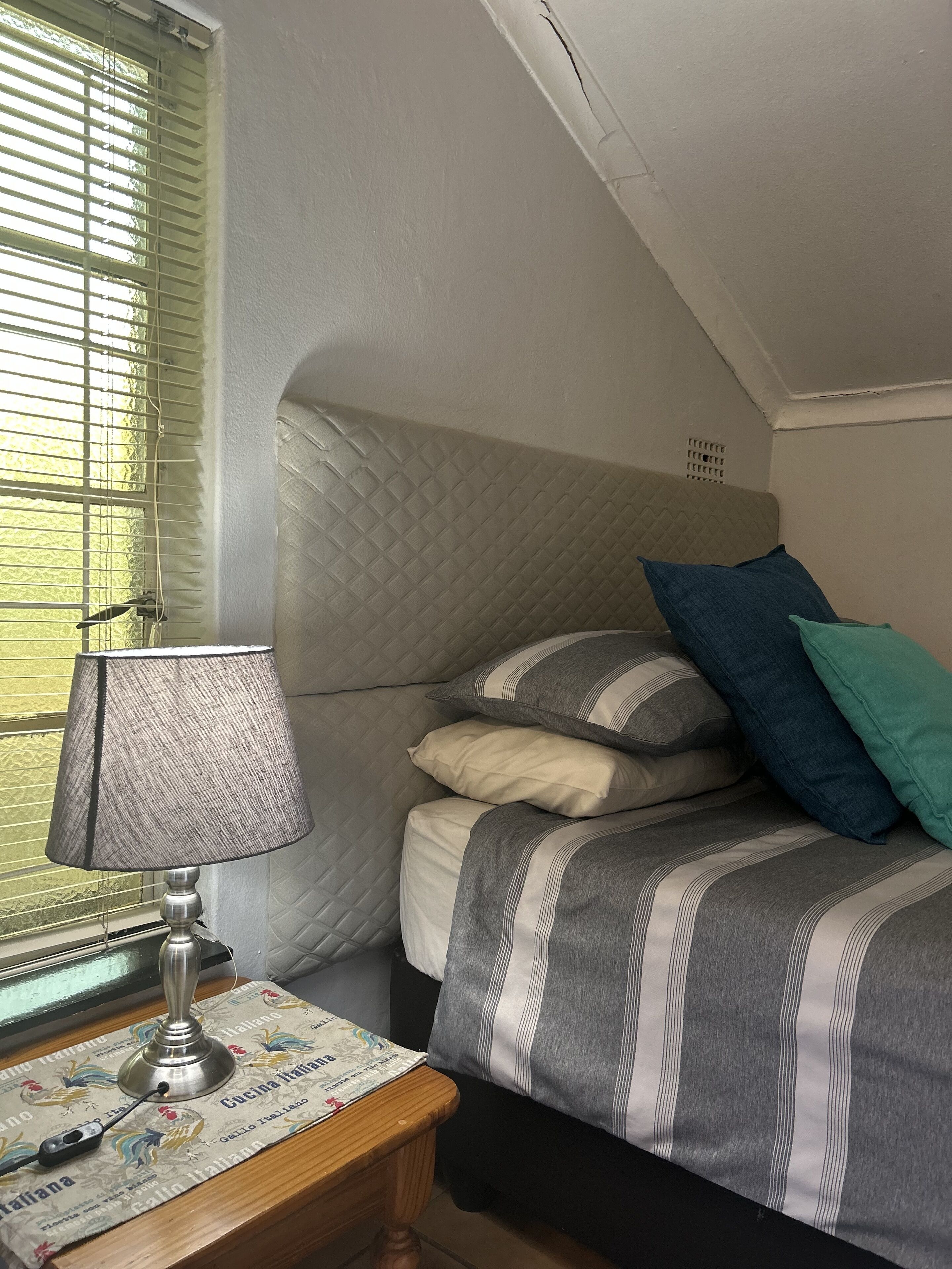 A bedroom with a bed, pillows, a lamp, and a table with a decorative cloth.