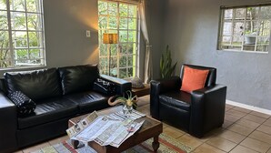 A living room with a black leather sofa, a wooden coffee table with maps, and a black armchair with a red pillow.