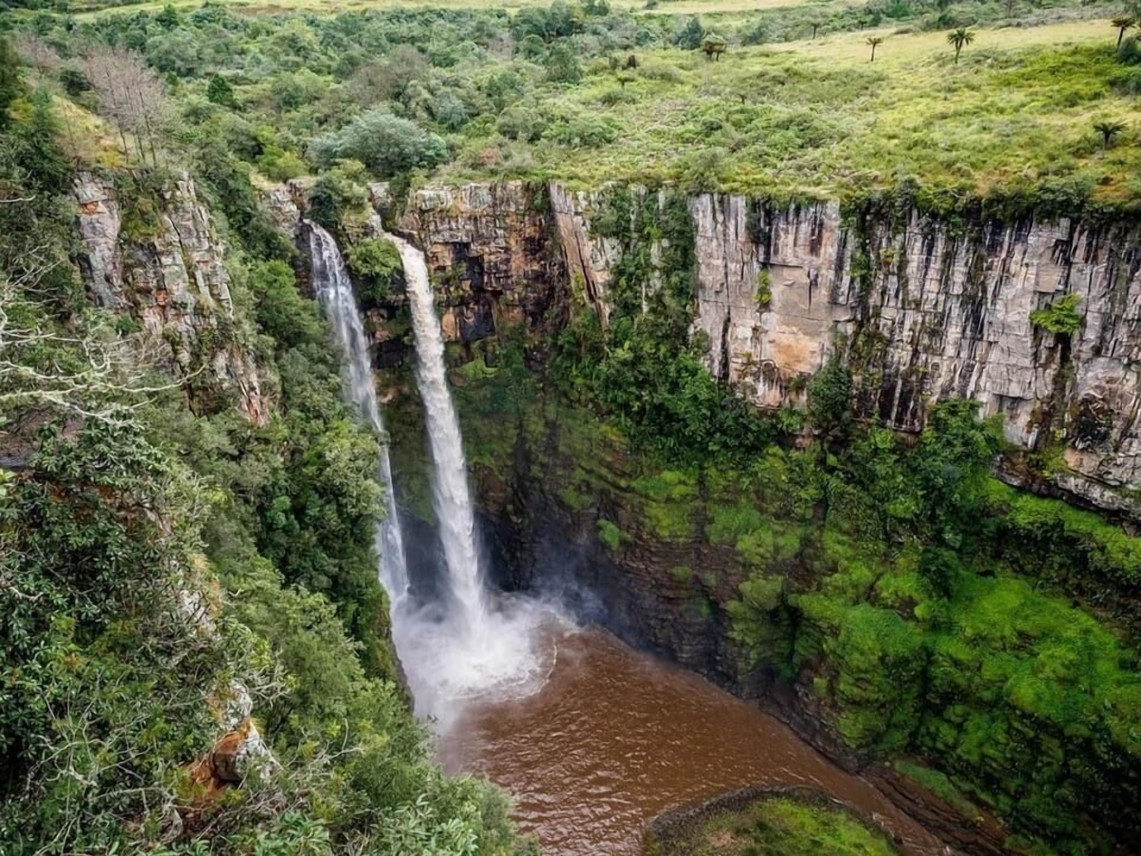 A waterfall cascading down a steep cliff surrounded by lush greenery.