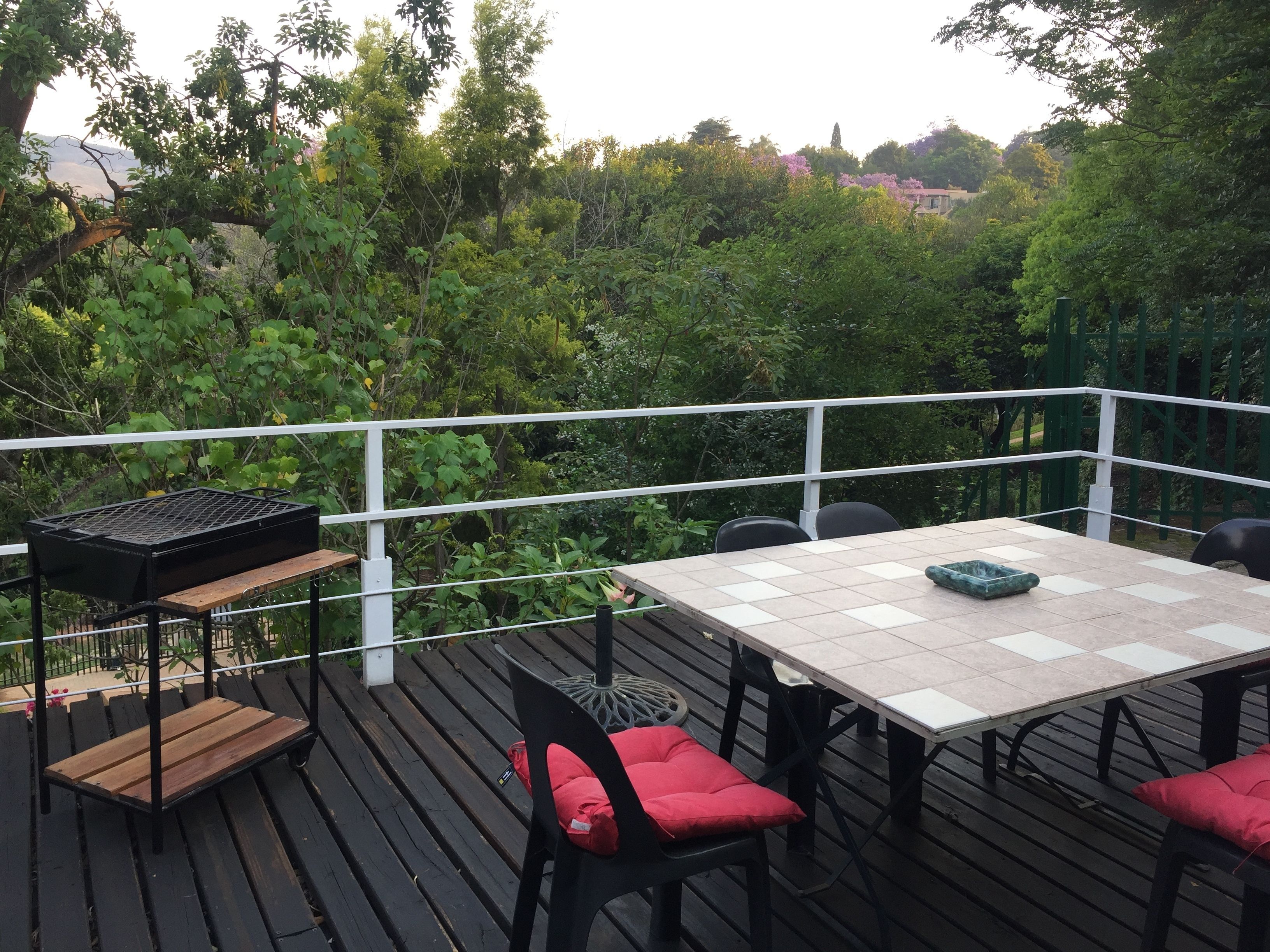 Una terrazza esterna con tavolo e sedie, immersa nel verde e dotata di ringhiera.