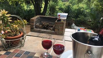 Un patio exterior con un brasero de ladrillo, dos copas de vino, un cubo de metal y una planta en maceta.