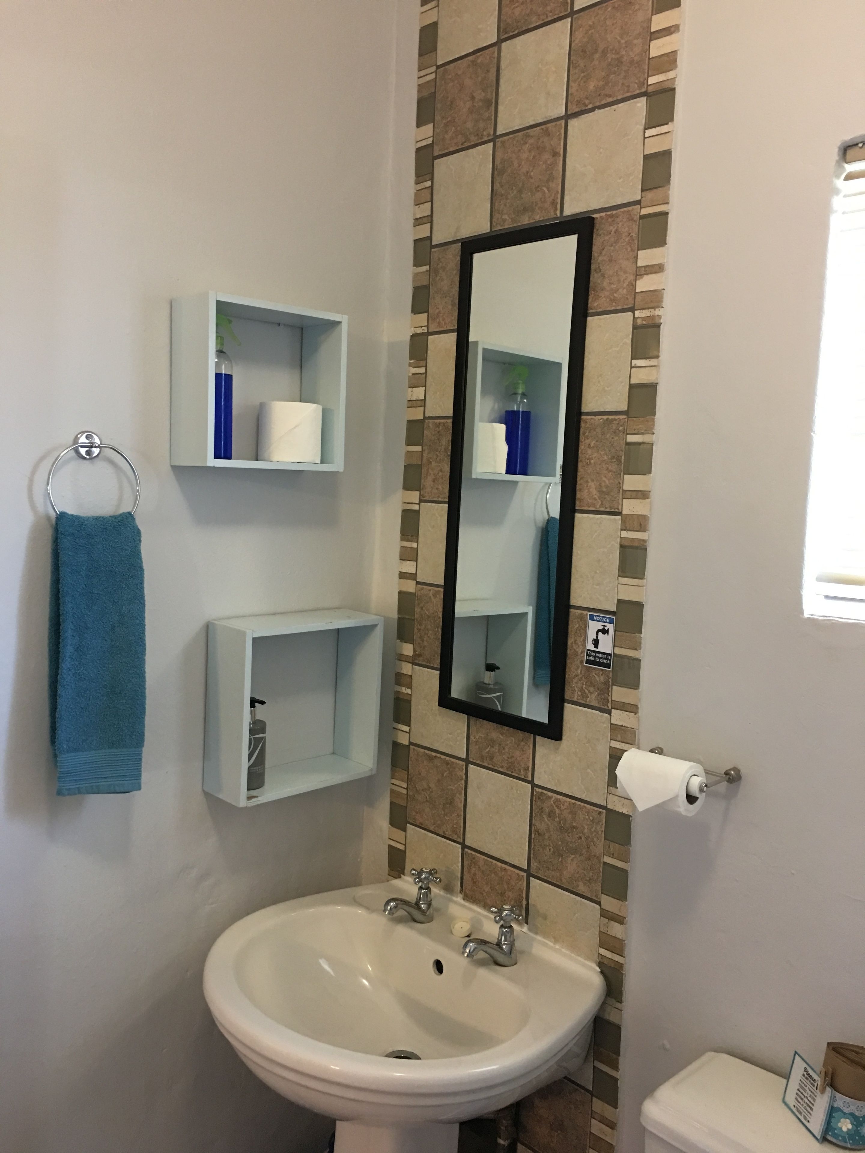 A bathroom with a sink, toilet, and two shelves with toiletries.