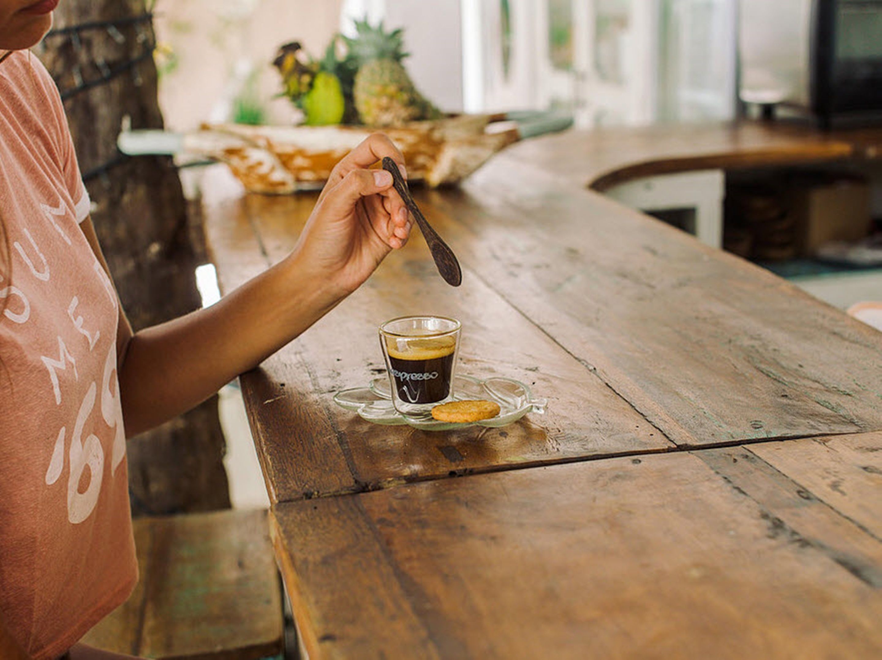 Una persona tiene un cucchiaio sopra una tazza di caffè su un tavolo di legno.