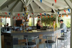 Ein überdachter Außenbereich mit Bar, Stein-Arbeitsplatten, Barhocker und einem Barkeeper.
