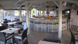 Een terras met witte stoelen en tafels, een bar in het midden en een overdekt zitgedeelte.