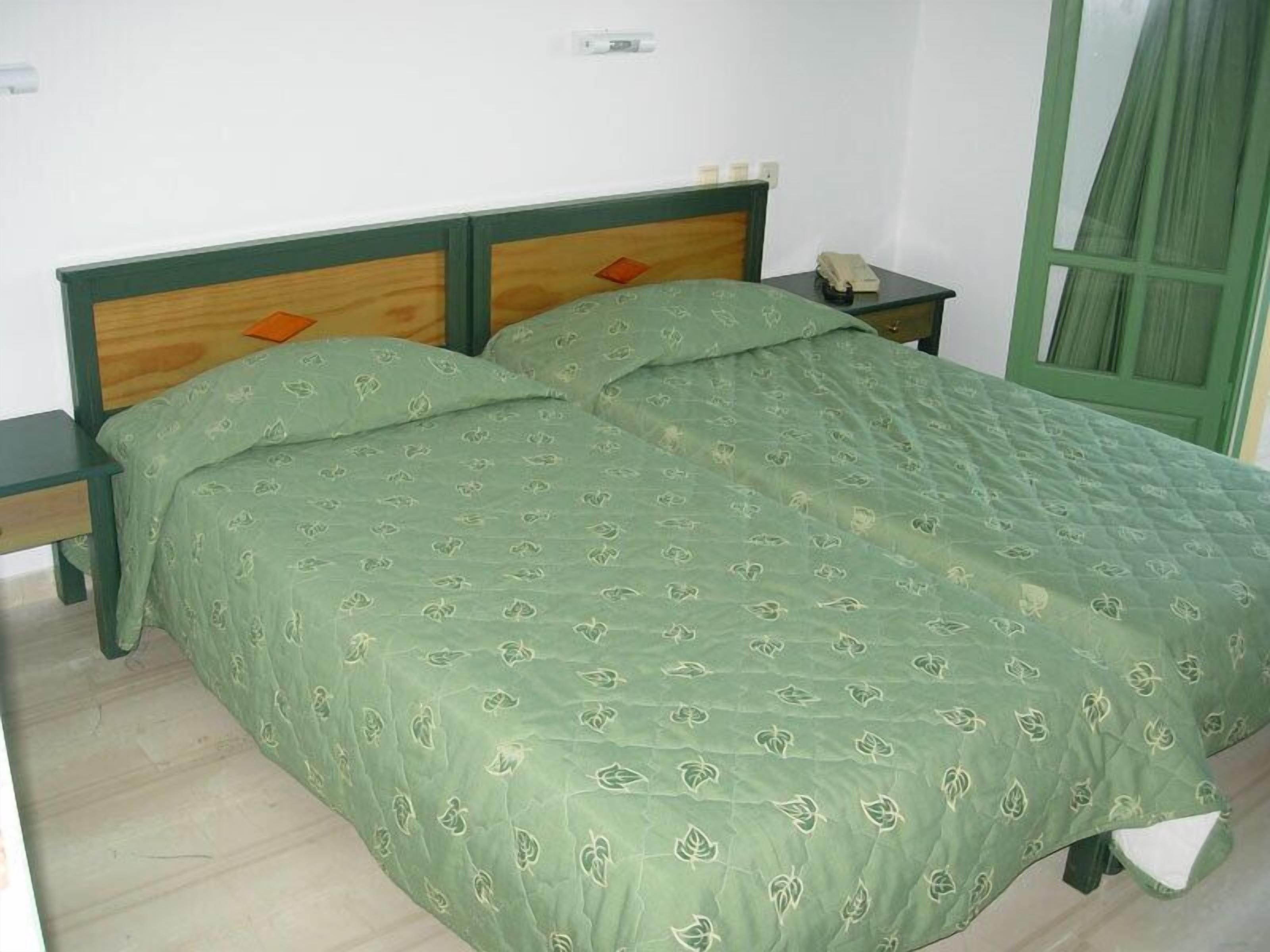 A single-bed room with a green bedspread, wooden headboard, and a nightstand with a telephone.