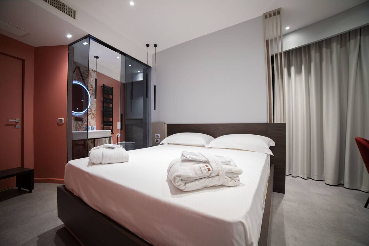 A hotel room with a bed, a mirror, a red bench, and a red chair.