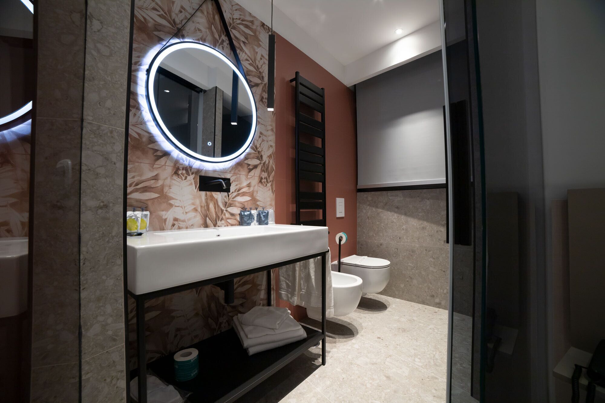 Ein modernes Badezimmer mit rundem Spiegel, weißem Waschbecken und zwei Toiletten.