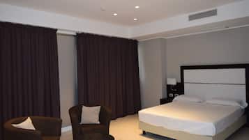 Una habitación de hotel con cama, una silla, una mesita de noche y un ventanal con cortinas.