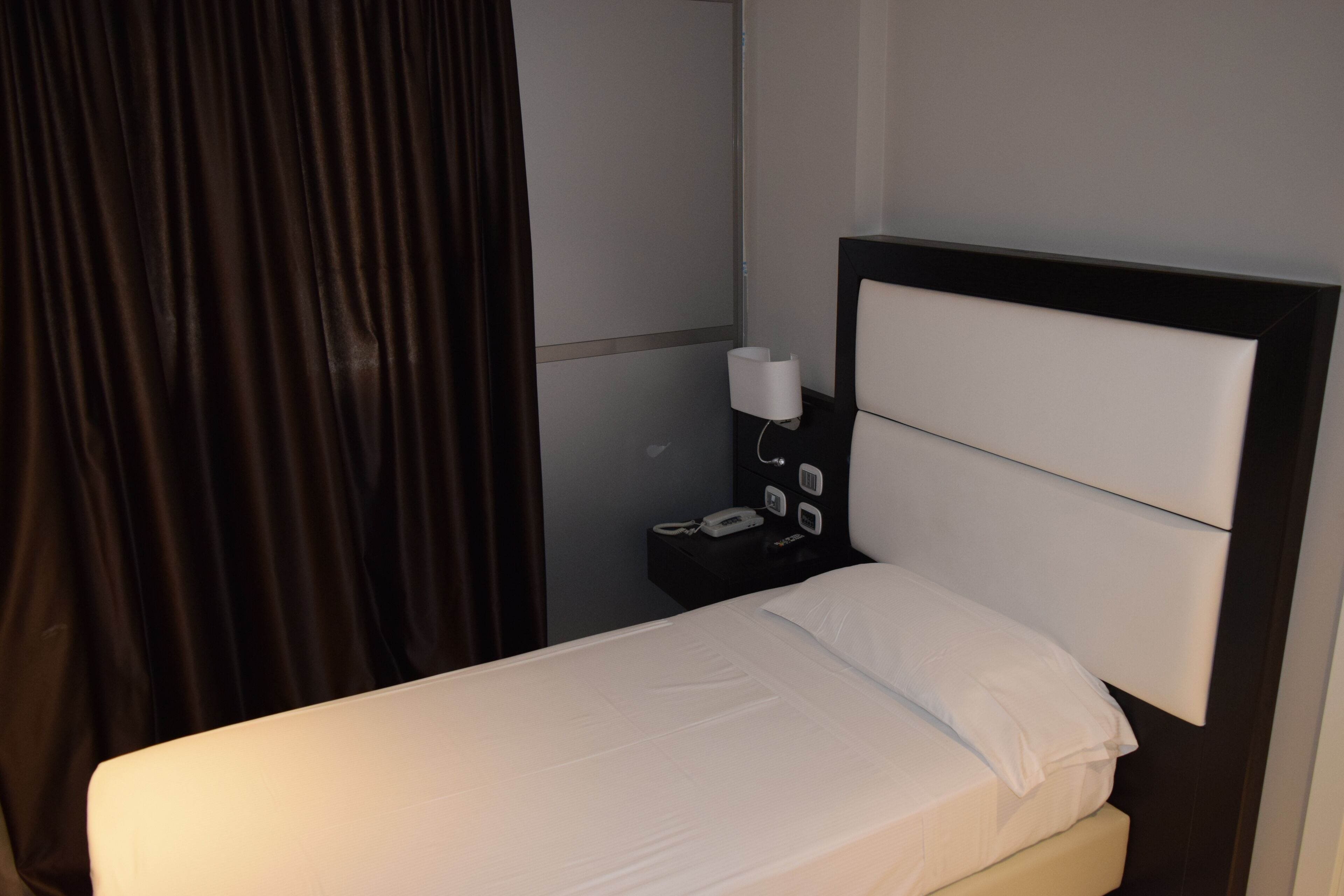 Una camera d'albergo con un letto, un comodino con il telefono e una lampada a parete.
