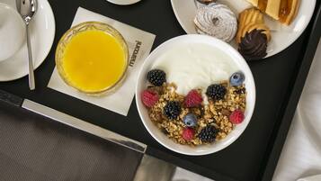 Bandeja de desayuno con yogur, granola, bayas, pastelería y un vaso de jugo de naranja.