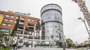 A modern building with a cylindrical glass facade, a visible entrance, and a sign for 'Marconi'.