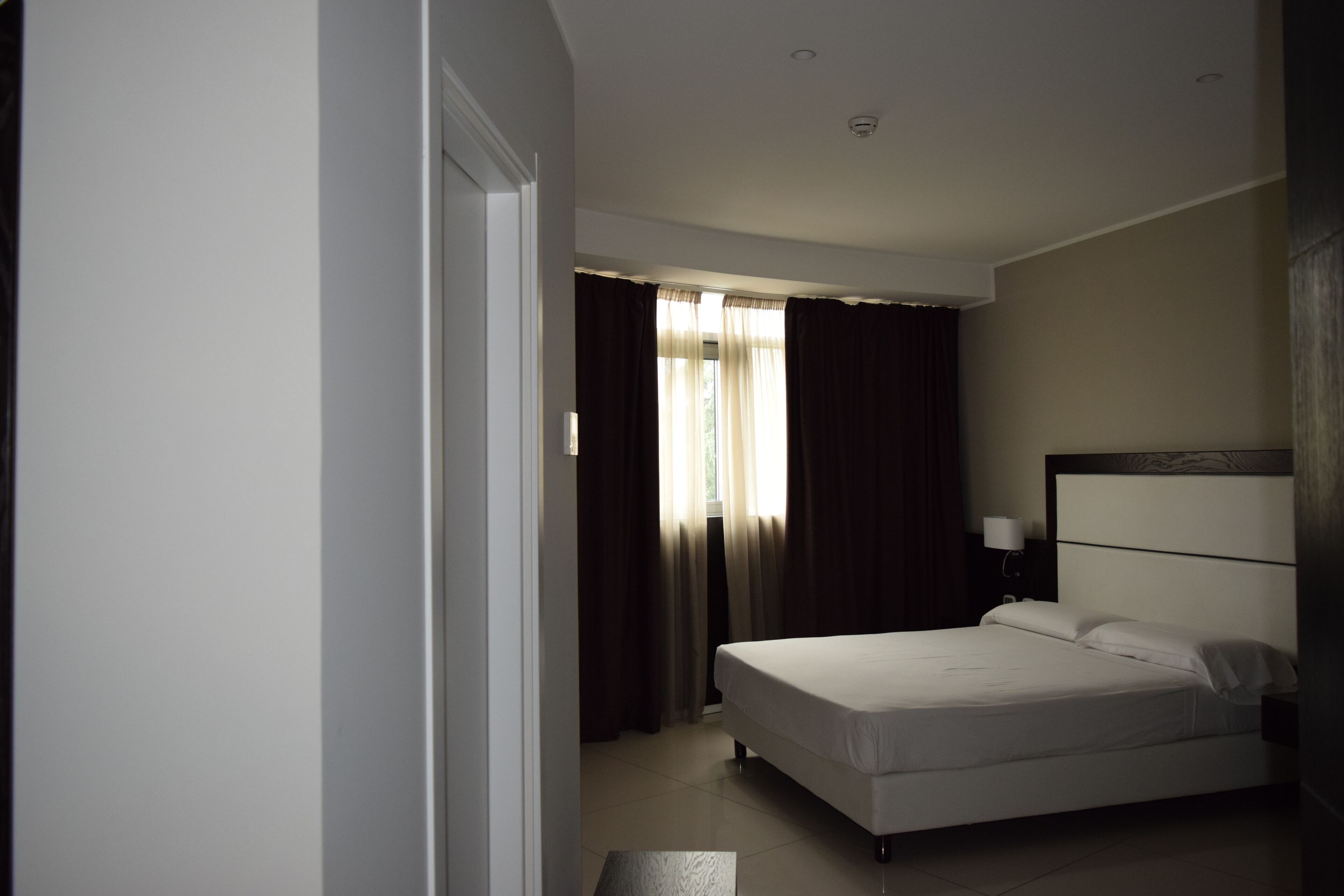 Un dormitorio con una cama individual, una mesita de noche con lámpara y una ventana con cortinas.