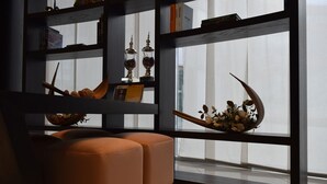 A modern living room with a sofa, shelves with decorative items, and a large window with sheer curtains.