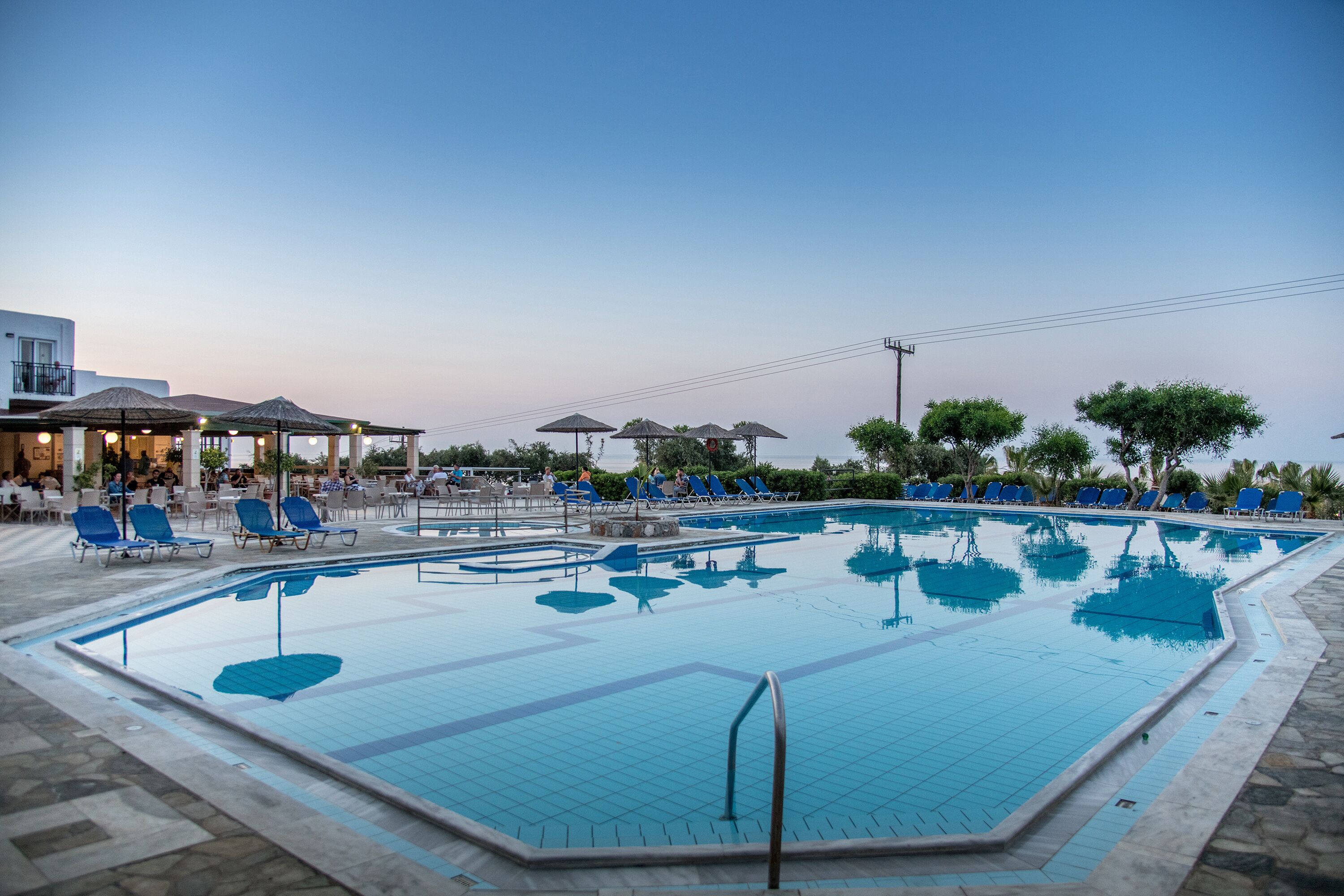 A swimming pool with blue tiles, surrounded by lounge chairs and umbrellas.