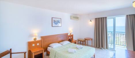 Habitación de hotel con cama, mesitas de noche de madera, escritorio, silla y balcón con cortinas.