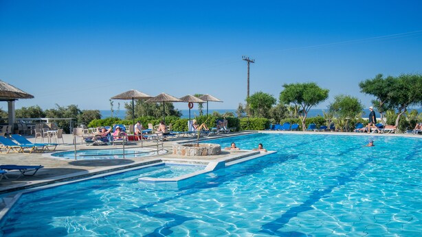 A swimming pool with lounge chairs and umbrellas, surrounded by trees and a view of the sea. - Semiramis Village (Hersonissos)