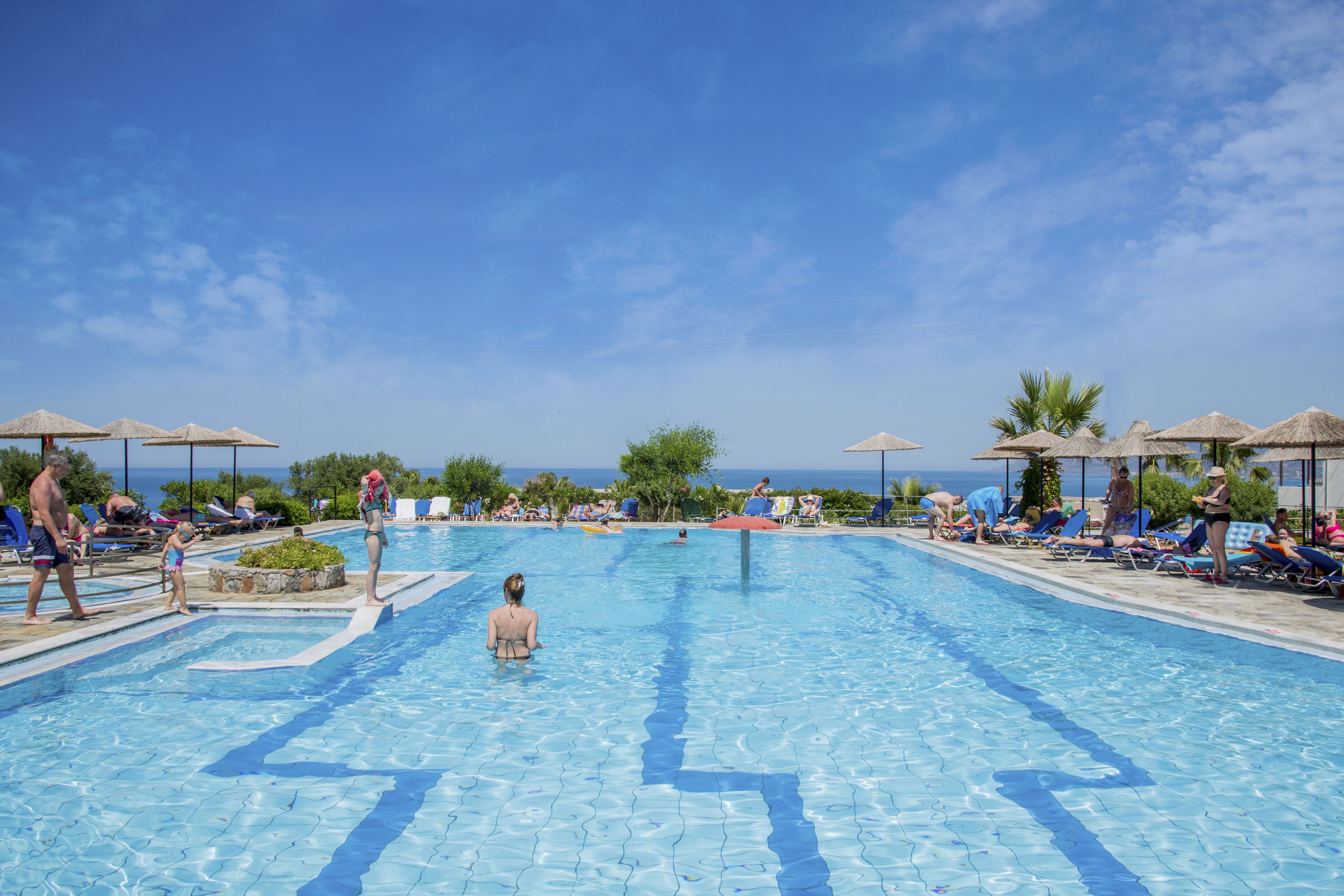 Piscina com água azul cristalina, rodeada por espreguiçadeiras e guarda-sóis, com vista para o mar ao fundo.