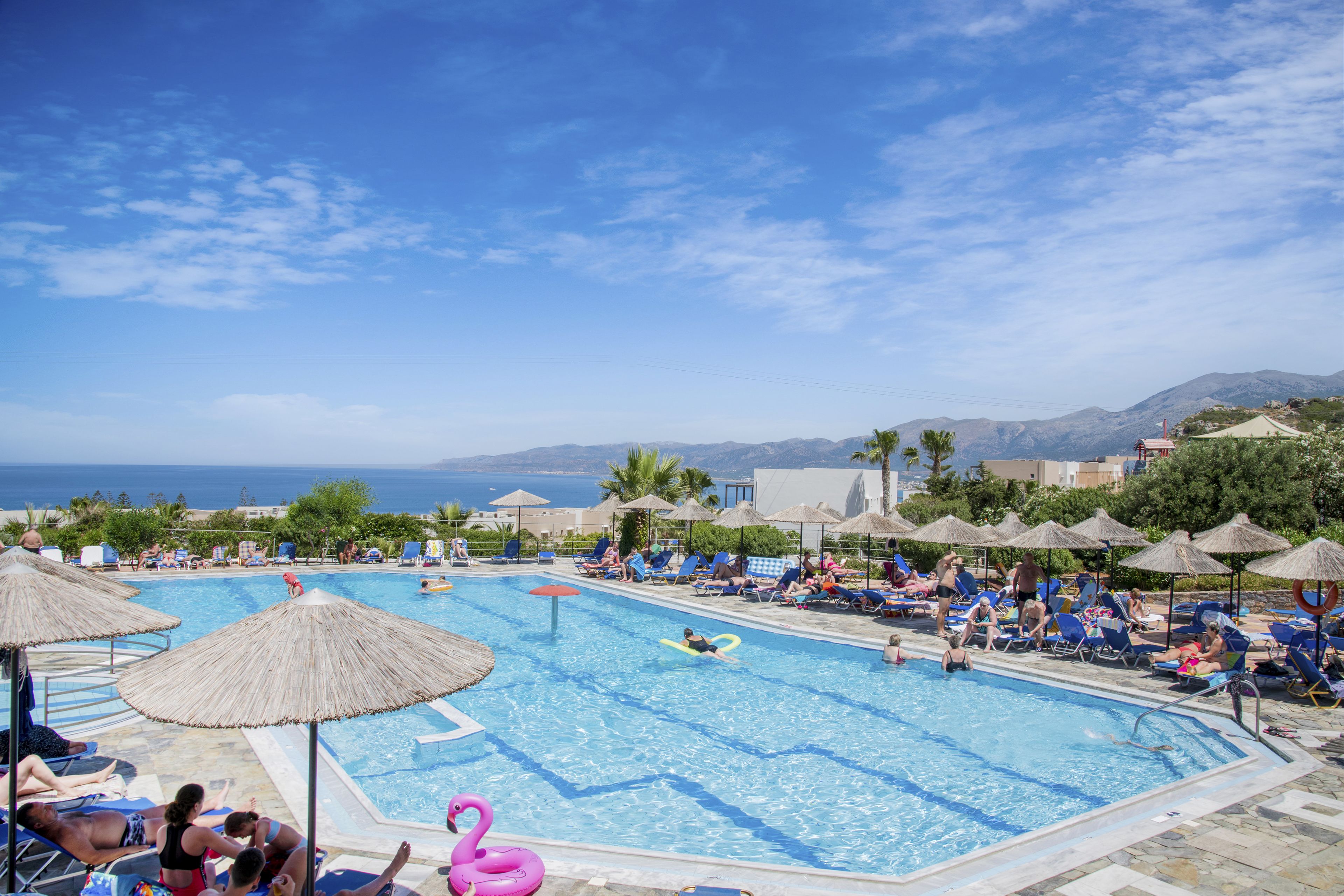 A pool area with lounge chairs and umbrellas, surrounded by mountains and the sea.