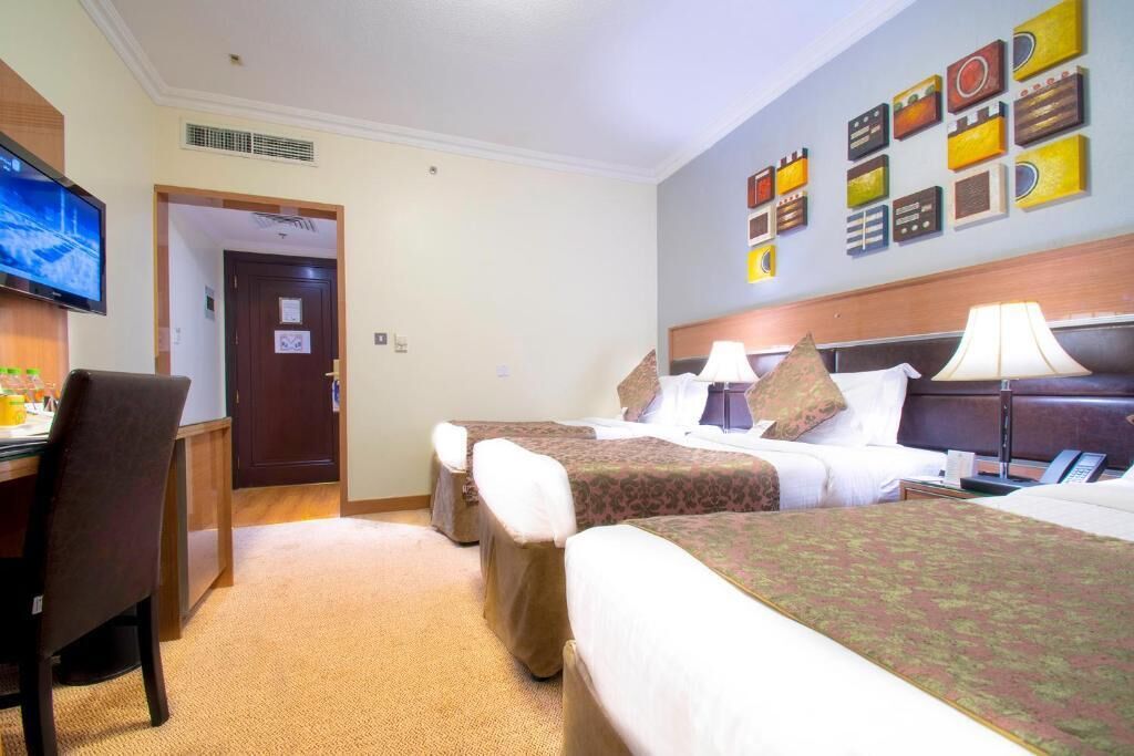 Habitación de hotel con dos camas, un escritorio, un televisor y una pared decorada con cuadros.