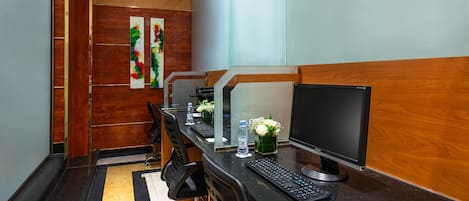 A hotel room with a long desk, multiple monitors, a keyboard, a water bottle, and a vase with flowers.
