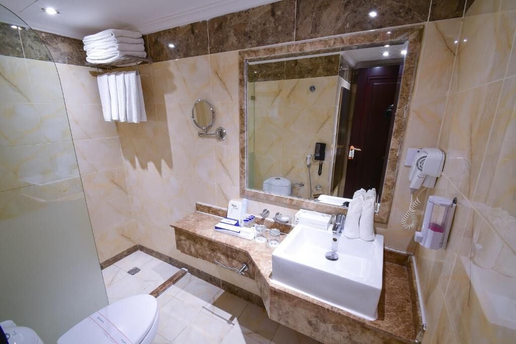 A modern bathroom with a marble vanity, a large mirror, a toilet, and a shower area.