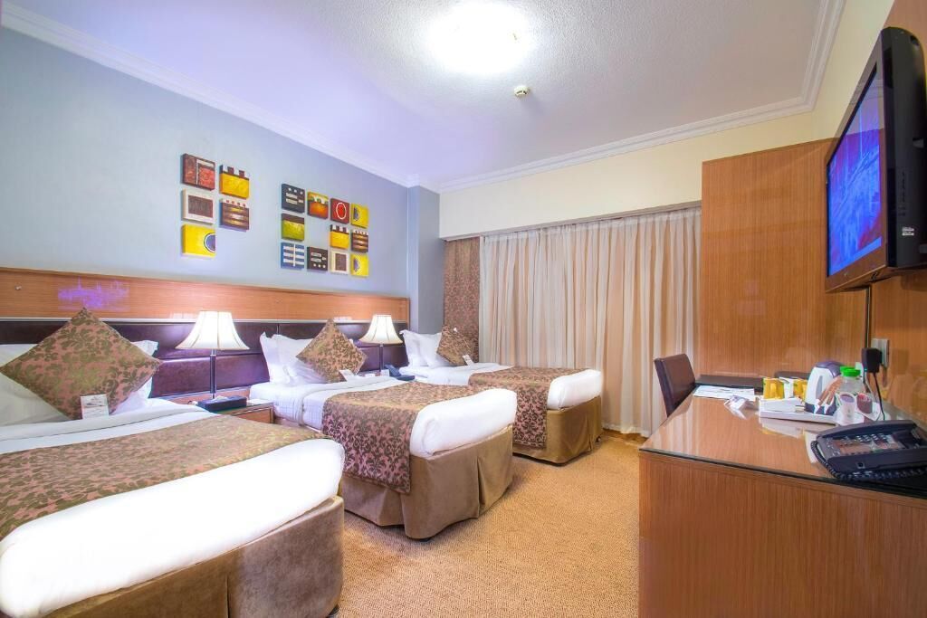 Ett hotellrum med två sängar, ett skrivbord, en tv och en vägg med inramade tavlor.
