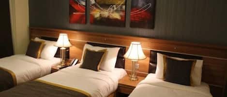 A hotel room with two beds, each with a lamp and a telephone. There are abstract paintings on the wall above the beds.
