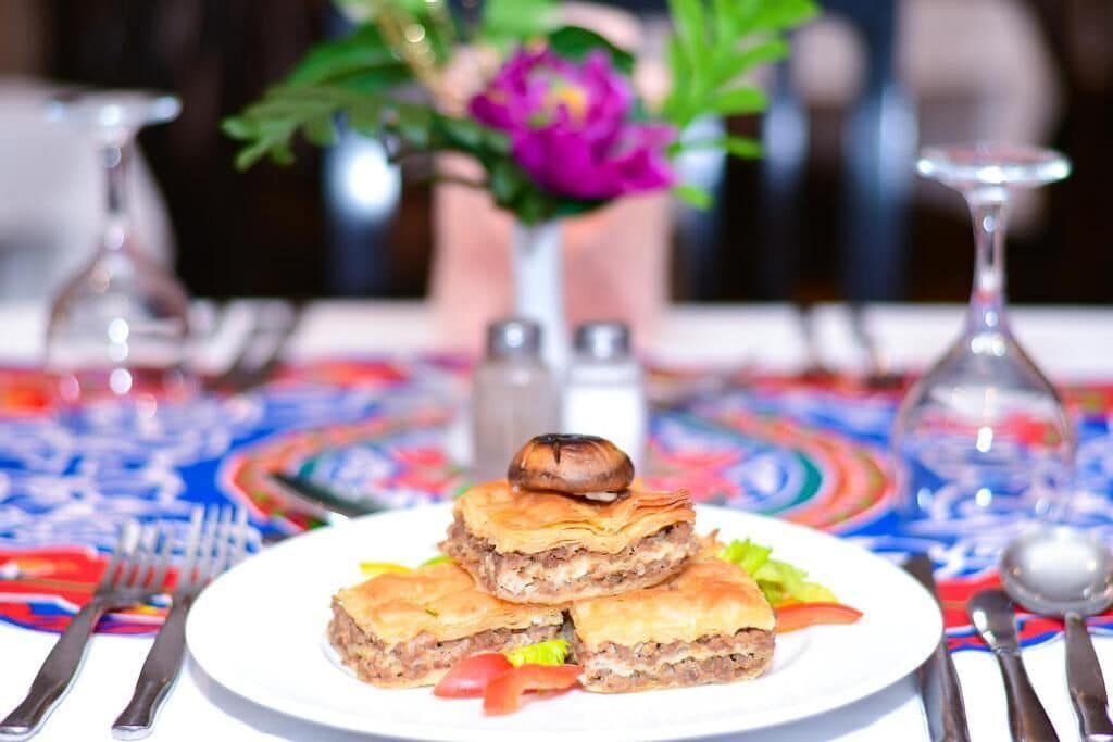 A plate of stuffed pastries with a mushroom on top, garnished with lettuce and tomato slices, on a colorful tablecloth.