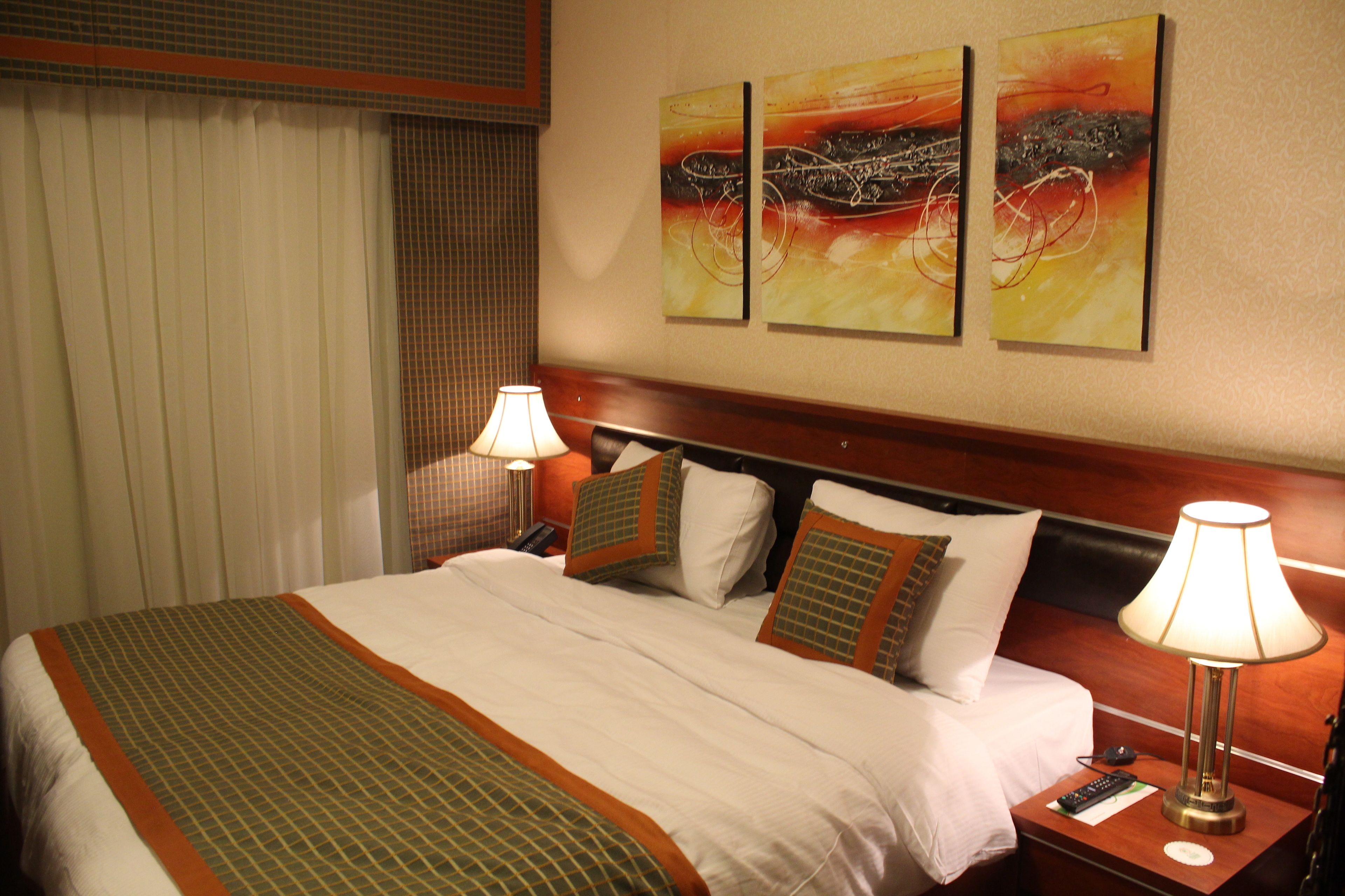 A hotel room with a large bed, two bedside tables, a nightstand, and a wall with three abstract paintings.