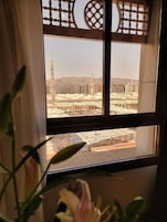 A view of a large mosque with multiple minarets and a courtyard through a window with a decorative grille.