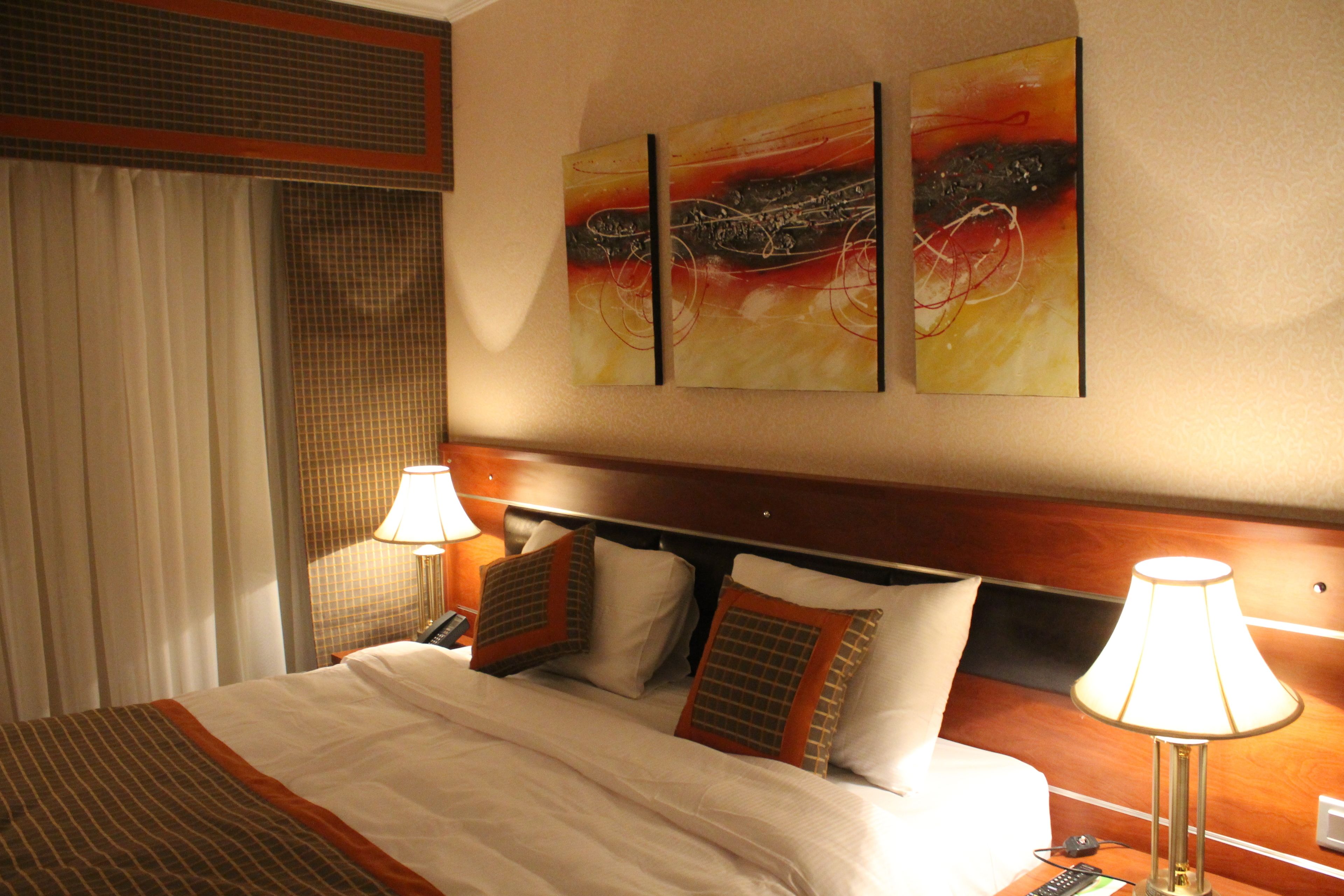 Habitación de hotel con una cama, dos lámparas de noche, un teléfono y una obra de arte en la pared.