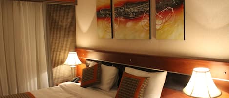 A hotel room with a bed, two bedside lamps, a telephone, and a wall-mounted artwork.