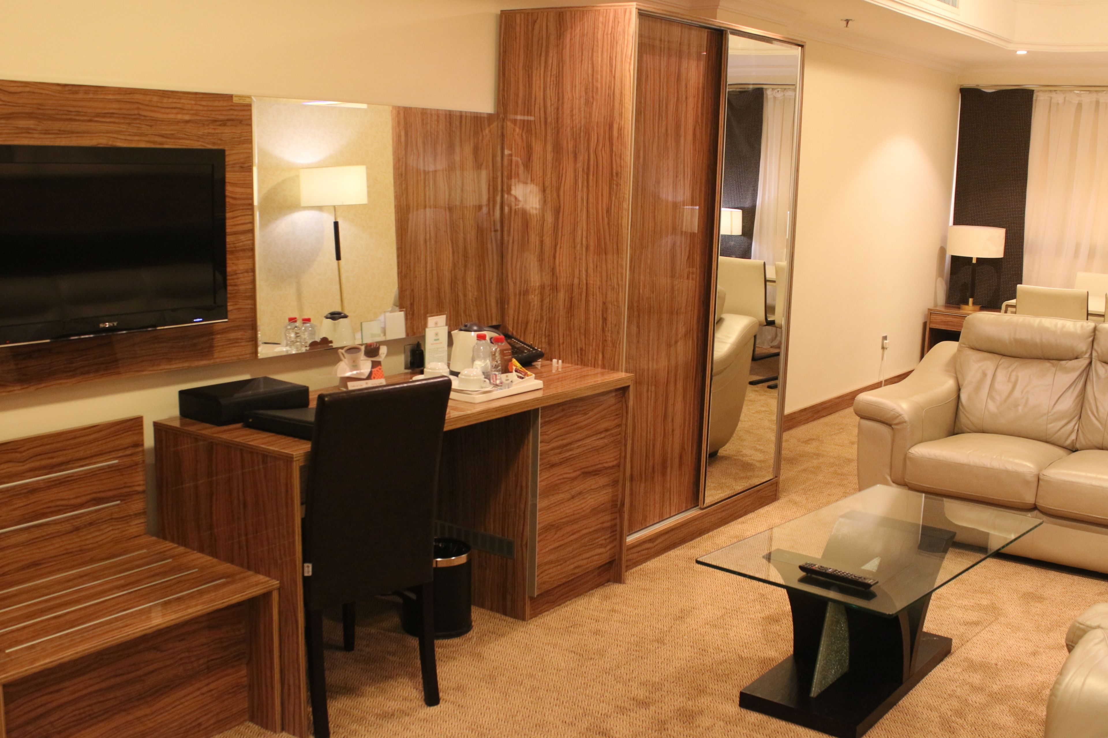Een hotelkamer met een houten bureau, een televisie, een bank en een glazen bijzettafeltje.