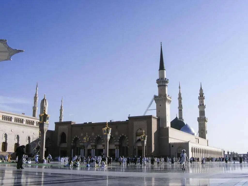 A large mosque with multiple minarets and a central dome, surrounded by a spacious courtyard with people.