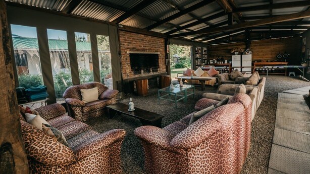 A cozy outdoor living area with a brick fireplace, comfortable seating, and a view of the surrounding landscape. - The Village Lodge (Storms River)