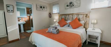 A bedroom with a bed, two nightstands, a dresser, a bathroom visible through an open door, and artwork on the walls.