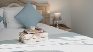 A neatly made bed with a stack of folded towels and a glass of water on the side. - The Village Lodge (Storms River)