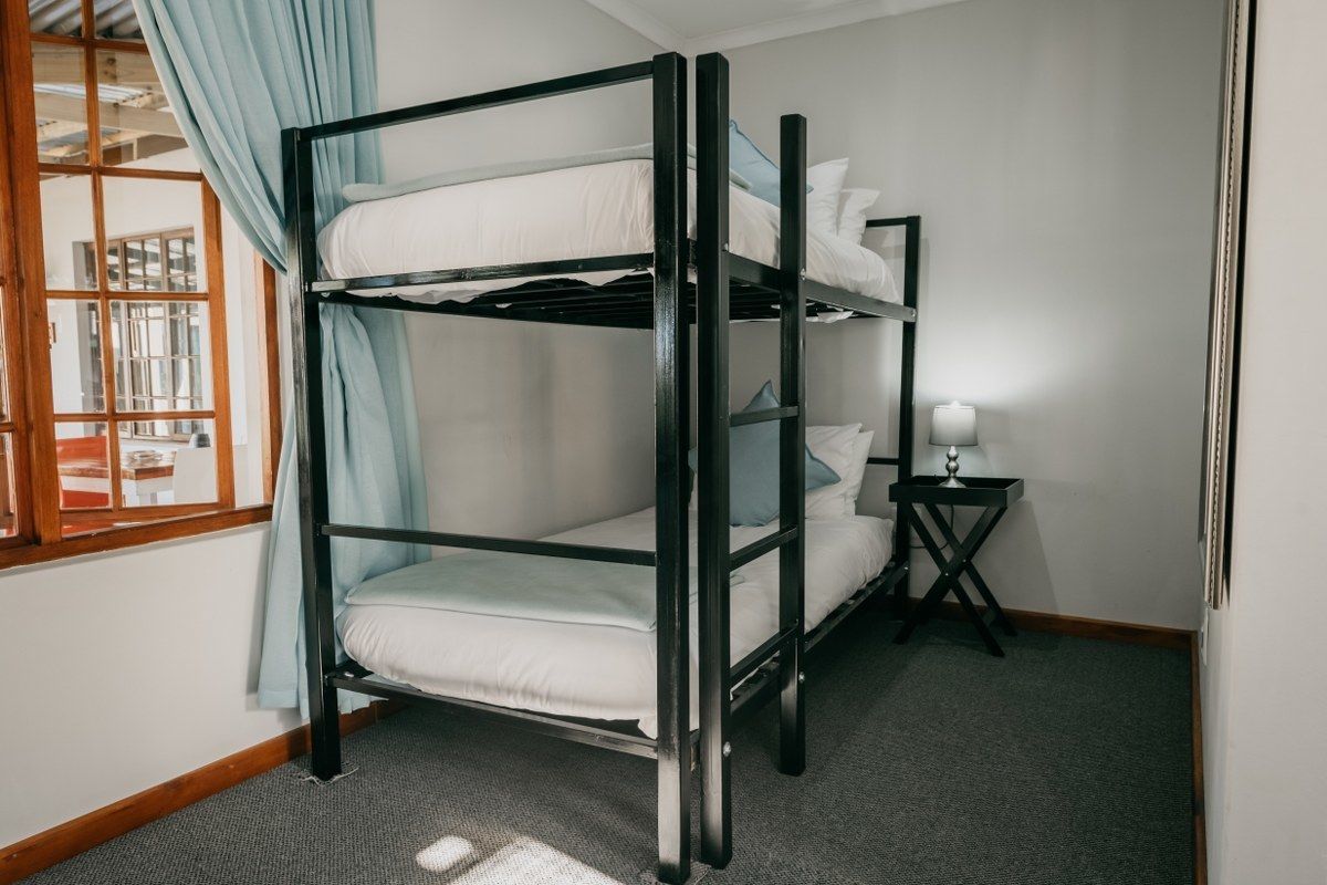 A bunk bed room with a window, a small table with a lamp, and a carpeted floor.