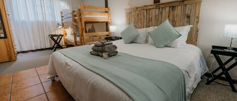 Un dormitorio con una cama grande, cabecero de madera y una cama litera adosada a la pared.